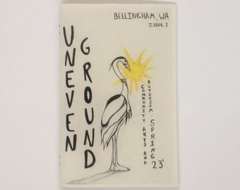 May include: A magazine cover with the title "Underground" in black text. The cover features a black and white illustration of a heron standing in front of a yellow sun. The text "Bellingham, WA Issue 1" is at the top of the cover. The text "Bellingham, WA - Spring '23 Community Arts and Activities" is on the right side of the cover.