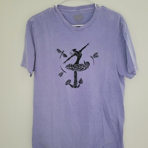Könnte beinhalten: Ein lavendelfarbenes T-Shirt mit einer schwarzen Grafik einer Person, die auf einem Pilz mit einer Schnecke und Libellen steht.