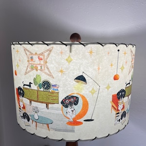 May include: A white lampshade with a black and white illustration of dogs in a mid-century modern living room. The lampshade has a black trim and a wooden finial.