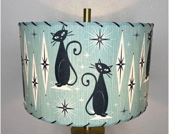 May include: A blue and white lampshade with a black cat design. The lampshade has a diamond pattern and stars. The cats are stylized and have a retro look.