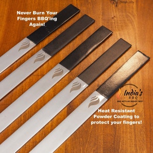 May include: Five metal skewers with black heat-resistant powder coating to protect fingers while grilling. The skewers are arranged on a wooden surface. The text "Never Burn Your Fingers BBQ'ing Again!" and "Heat Resistant Powder Coating to protect your fingers!" is visible in the image.