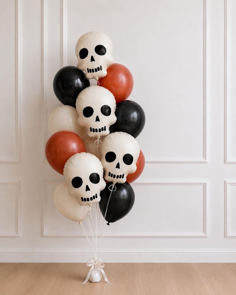 May include: A balloon bouquet featuring three off-white skull-shaped balloons with black facial features, interspersed with round balloons in solid black, burnt orange, and cream colors, all tied together with white ribbons at the base.
