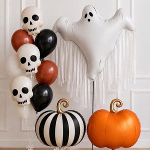May include: A collection of Halloween balloons including a large white ghost balloon with fringe, two pumpkin-shaped balloons in orange and black-and-white stripes, and a cluster of skull-shaped balloons mixed with solid black and orange round balloons.