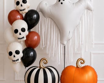 May include: A collection of Halloween balloons including a large white ghost balloon with fringe, two pumpkin-shaped balloons in orange and black-and-white stripes, and a cluster of skull-shaped balloons mixed with solid black and orange round balloons.