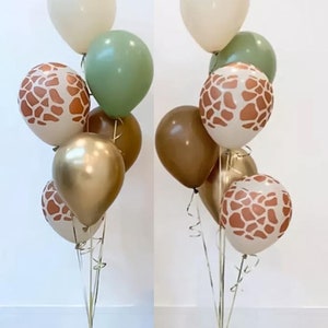 May include: A balloon bouquet featuring a mix of solid cream, sage green, and dark brown balloons, alongside metallic gold balloons and cream balloons with a brown giraffe print pattern. The balloons are tied with gold ribbons to a small gold base.
