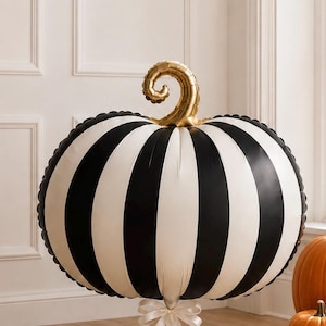 May include: A large, round, inflatable pumpkin balloon featuring vertical black and white stripes. The pumpkin has a metallic gold, spiraled stem at the top and is tied at the base with a white ribbon. The surface has a smooth, glossy finish.