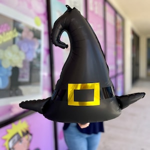 Può includere: Un palloncino a forma di cappello da strega nero con una fibbia dorata. Il palloncino è gonfiato e pronto per essere utilizzato per una festa di Halloween.