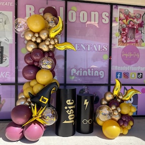 May include: A balloon arch with gold and burgundy balloons, a witch hat, and a golden lightning bolt. The arch is in front of a store window with the words "Ready 4 Your Party" and "@Ready4YourParty" on it. There are two black pillars with the words "Josie" and "4" on them.