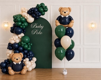 May include: A balloon display featuring a dark green arched backdrop with the text Baby Polo, decorated with a large garland of dark green, navy blue, and cream balloons, two teddy bear foil balloons, and a cluster of matching helium balloons.