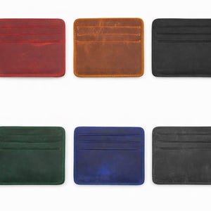 May include: Six leather cardholders in various colors: red, brown, black, green, blue, and gray. Each cardholder has a rectangular shape with rounded corners and multiple card slots. The cardholders are displayed on a white background.
