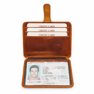 May include: Open brown leather wallet with three credit card slots and a clear ID window. The wallet displays an Arizona driver's license. The wallet has a tab closure.