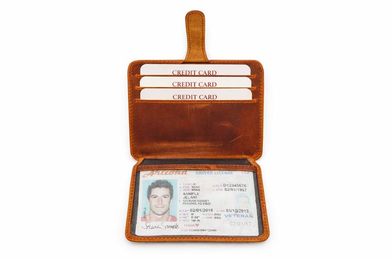 May include: Open brown leather wallet with three credit card slots and a clear ID window. The wallet displays an Arizona driver's license. The wallet has a tab closure.