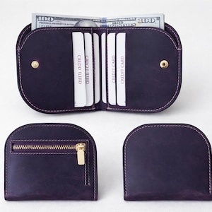K&ouml;nnte beinhalten: Ein Set aus drei dunkelvioletten Ledergeldb&ouml;rsen. Eine Geldb&ouml;rse ist ge&ouml;ffnet und zeigt Kreditkarten und einen Stapel 100-Dollar-Scheine. Die anderen beiden Geldb&ouml;rsen sind geschlossen, eine mit Rei&szlig;verschluss und goldfarbener Hardware.