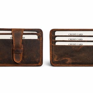 May include: Two brown leather cardholders. One has a flap with a buckle closure, the other has three card slots. Each cardholder has white cards with "CREDIT CARD" printed on them.