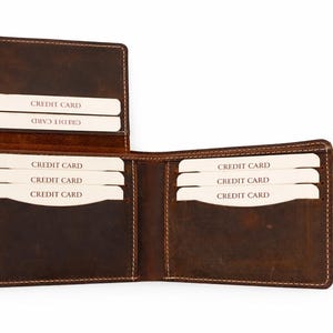 May include: Open brown leather wallet with multiple card slots. The wallet is open, revealing several white credit cards. The leather has a distressed look, with visible stitching around the edges. The wallet is designed to hold credit cards.