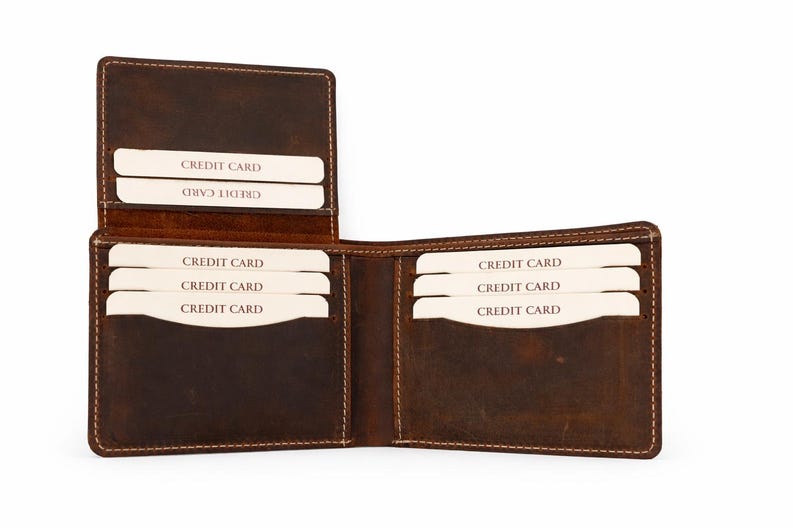 May include: Open brown leather wallet with multiple card slots. The wallet is open, revealing several white credit cards. The leather has a distressed look, with visible stitching around the edges. The wallet is designed to hold credit cards.