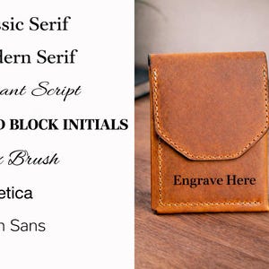 May include: A brown leather wallet with a flap closure, featuring the text "Engrave Here" on the front. The image also displays a list of font styles, including "Classic Serif" and "Bold Block Initials".