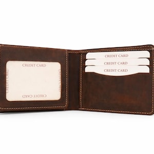 May include: Open brown leather wallet with visible stitching. The wallet is open, revealing slots for credit cards. The cards are white with the words "CREDIT CARD" printed on them. The wallet is empty except for the cards.