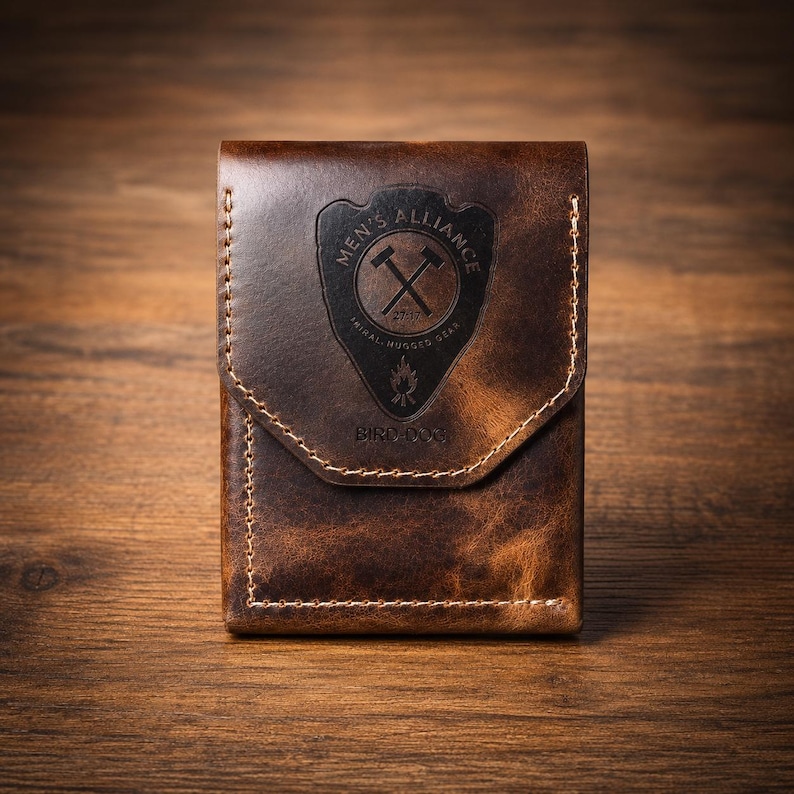 May include: A brown leather wallet with a flap closure. The wallet features a stitched design and a black emblem with the text "MEN'S ALLIANCE" and "BIRD DOG". The wallet is made of distressed leather.