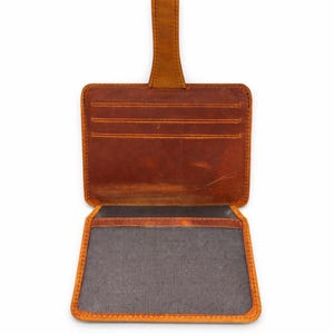 May include: Open, brown leather wallet with a pull tab. The wallet has multiple card slots and a large compartment. The edges are a lighter shade of brown, and the interior is lined with a gray fabric.