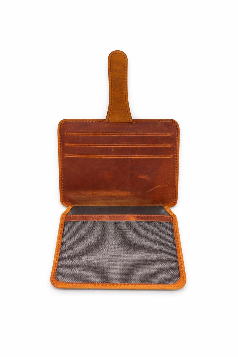May include: Open, brown leather wallet with a pull tab. The wallet has multiple card slots and a large compartment. The edges are a lighter shade of brown, and the interior is lined with a gray fabric.