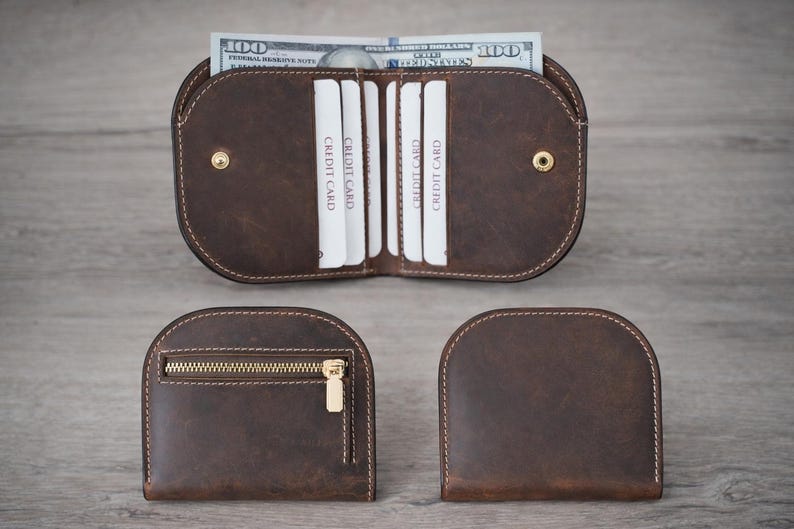 K&ouml;nnte beinhalten: Ein Set aus drei braunen Ledergeldb&ouml;rsen. Eine Geldb&ouml;rse ist ge&ouml;ffnet und zeigt Kreditkartenf&auml;cher und einen 100-Dollar-Schein. Die anderen beiden Geldb&ouml;rsen sind geschlossen, eine mit Rei&szlig;verschluss.