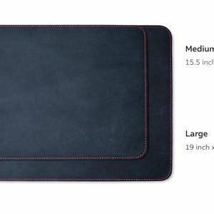 May include: Two dark blue rectangular desk mats with red stitching. The medium mat measures 15.5 inches by 12 inches, and the large mat is 19 inches by 14 inches. The mats are displayed on a white background.