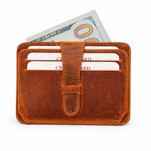 May include: A brown leather wallet with a flap closure, holding several white credit cards and a US $100 bill. The wallet has a rectangular shape and a textured surface, with a vertical strap closure.