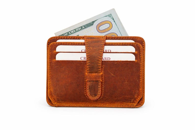 May include: A brown leather wallet with a flap closure, holding several white credit cards and a US $100 bill. The wallet has a rectangular shape and a textured surface, with a vertical strap closure.