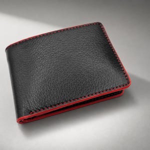 May include: A bi-fold wallet crafted from black textured leather, featuring prominent red stitching along the edges and a vibrant red interior lining visible at the seams. The wallet has a rectangular shape with rounded corners and a smooth finish.