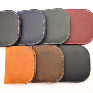 K&ouml;nnte beinhalten: Eine Sammlung von acht Ledergeldb&ouml;rsen in verschiedenen Farben, darunter Schwarz, Blau, Gr&uuml;n und Rot. Jede Geldb&ouml;rse hat eine abgerundete Form mit wei&szlig;en N&auml;hten an den Kanten. Die Geldb&ouml;rsen sind auf wei&szlig;em Hintergrund angeordnet.