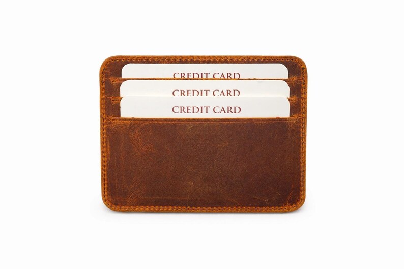 May include: A brown leather card holder with three white credit cards visible. The cards are labeled "CREDIT CARD" in a bold, red font. The card holder has a rectangular shape with rounded corners and a stitched border.