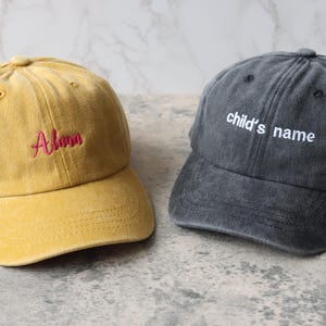 Puede incluir: Dos gorras de b&eacute;isbol, una amarilla con el nombre "Alana" bordado en rojo, y una gris con el texto "child's name" bordado en blanco.