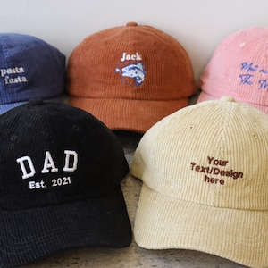 May include: Five corduroy baseball caps in different colours with embroidered text. The caps are blue, brown, pink, beige, and black. The text on the caps reads "eat pasta run fasta", "Jack", "What are we... The Will", "Your Text/Design here", and "DAD Est. 2021".