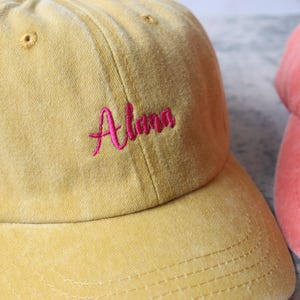Puede incluir: Una gorra de b&eacute;isbol amarilla con el nombre "Alena" bordado en rosa en la parte delantera.