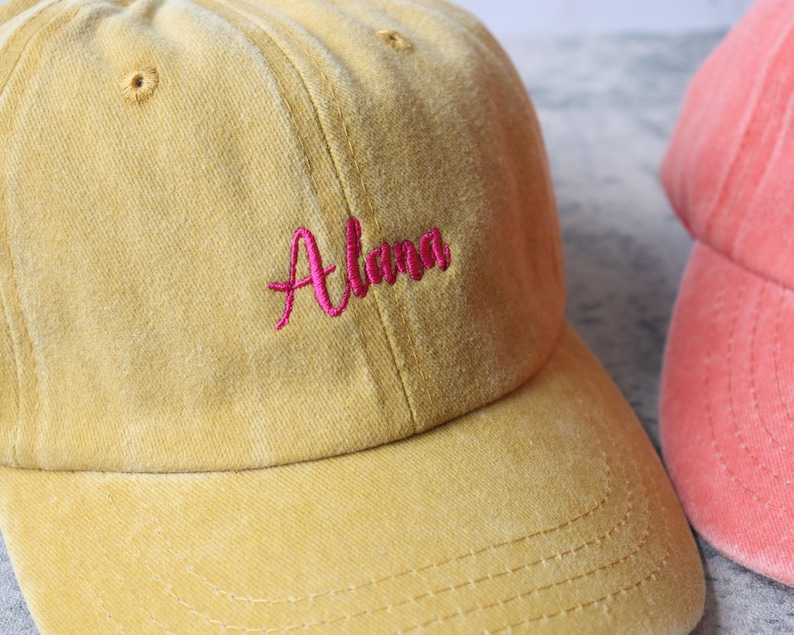 Puede incluir: Una gorra de b&eacute;isbol amarilla con el nombre "Alena" bordado en rosa en la parte delantera.