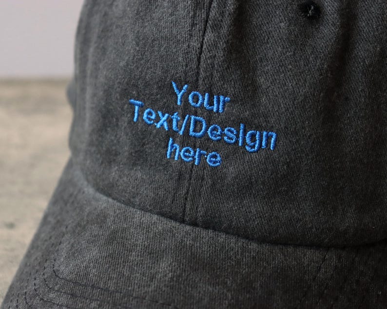 Pode incluir: Um bon&eacute; de beisebol cinza escuro com um design bordado azul que diz "Your Text/Design Here".