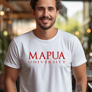 May include: White crew neck t-shirt with the red text "MAPUA UNIVERSITY". The shirt is short-sleeved and appears to be made of a soft material. The image is taken indoors, with a blurred background.