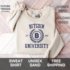 May include: A beige sweatshirt with the text "Bitcoin University" printed on the front. The text is in a navy blue color and is surrounded by a wreath with a Bitcoin symbol in the center. The text "EST 2008" is printed below the wreath.