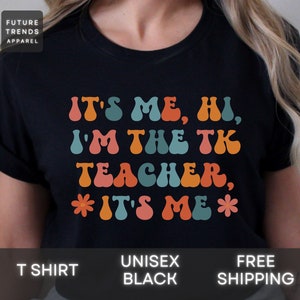 May include: Black t-shirt with a retro-style graphic that says "It's me, hi, I'm the TK teacher, It's me".