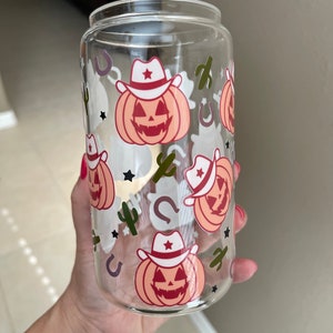 May include: A clear glass tumbler with a Halloween-themed design. The tumbler features a repeating pattern of orange pumpkins wearing cowboy hats, stars, horseshoes, and cacti.