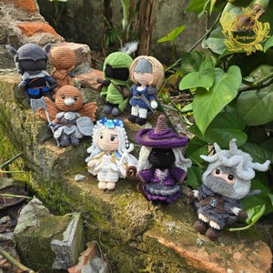以下が含まれることがあります： 手作りの編み人形のコレクション。それぞれがユニークなキャラクターデザインです。人形は、帽子、鎧、武器など、さまざまな衣装とアクセサリーを特徴としています。カラーパレットには、茶色、緑、青、紫、白の色合いが含まれています。
