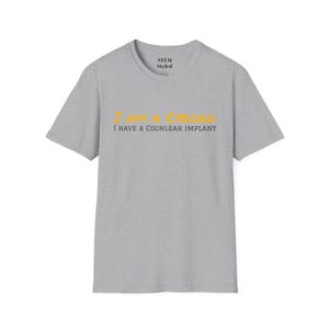 May include: A gray t-shirt with the text "I AM A CYBORG I HAVE A COCHLEAR IMPLANT" in yellow and black lettering.