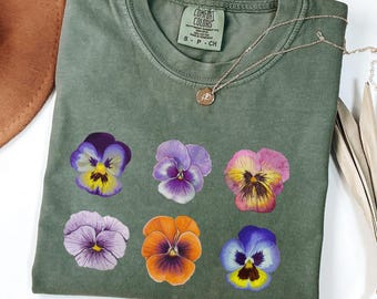 May include: A green t-shirt with a print of six purple, pink, and orange pansies. The shirt has a tag that says "Comfort Colors" and "S-P-CH".