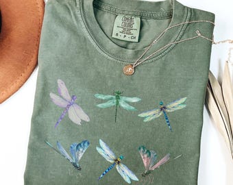 May include: A green t-shirt with a faded look featuring a pattern of colorful dragonflies. The shirt has a tag that reads "Comfort Colors" and "S - P - CH".