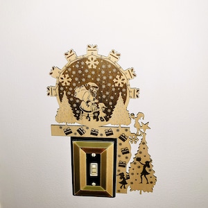 Puede incluir: Una cubierta de interruptor de luz de Navidad de madera con un diseño de Papá Noel y árbol de Navidad. La cubierta es marrón y tiene un interruptor de luz en el centro.
