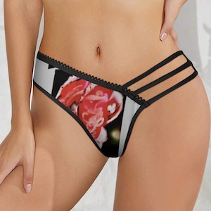 Może przedstawiać: Czarna i biała bielizna z kwiatowym nadrukiem przedstawiającym czerwoną i różową kwiat. Bielizna ma czarne wykończenie z falistą krawędzią i paskami po bokach.