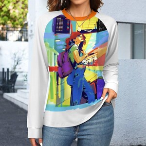 Könnte beinhalten: Weißes Langarm-Raglan-Shirt mit einer Illustration einer Person am Flughafen. Das Kunstwerk zeigt eine Frau mit Rucksack und Gepäck in leuchtenden Farben. Das Shirt hat einen orangefarbenen Ausschnitt.