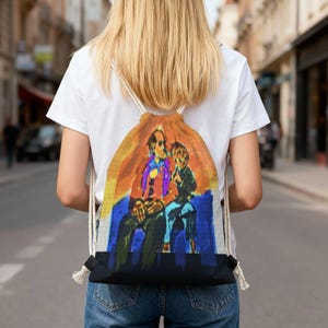 May include: A drawstring backpack featuring a colorful illustration of two figures. The artwork has a warm color palette with orange, yellow, and blue hues. The backpack has a black base and white drawstring cords.