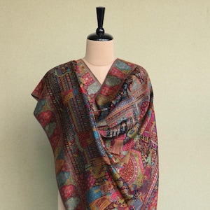 Puede incluir: Un chal colorido con un patrón de cachemira y detalles intrincados. El chal está drapeado sobre un maniquí y tiene una paleta de colores rica y vibrante.